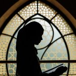 Silhouette of a woman reading in front of Islamic-patterned window. Peaceful and cultural ambiance.